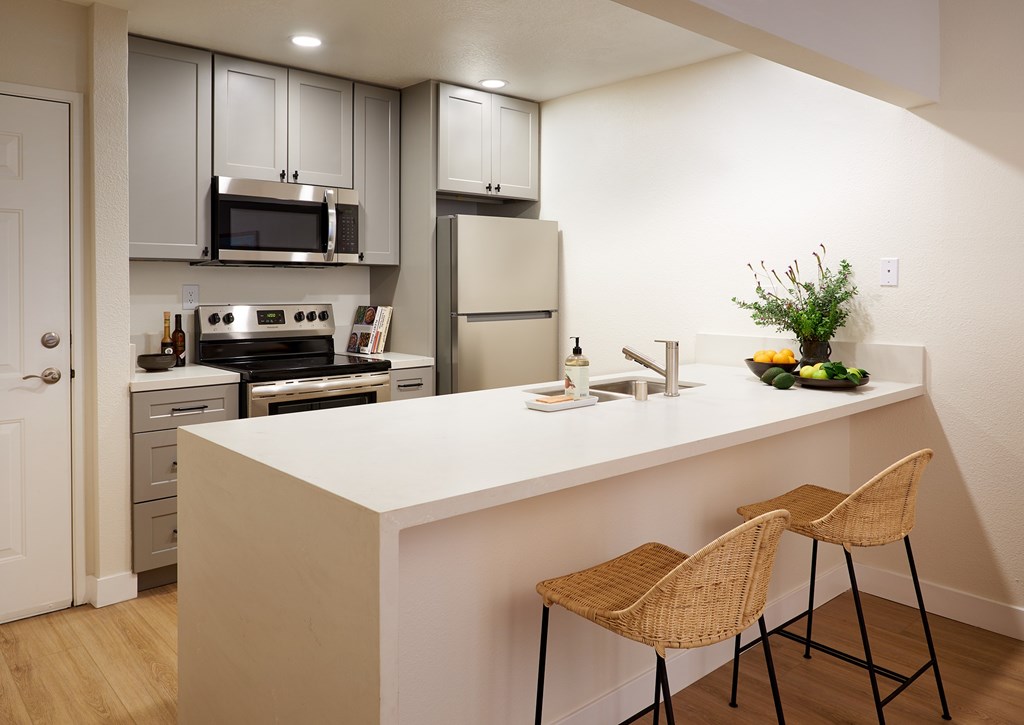 A kitchen with a white countertop and two wicker chairs.