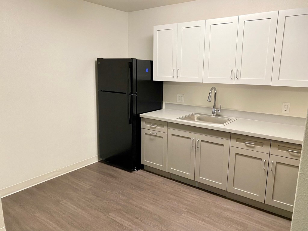 an empty kitchen with white cabinets and a black refrigerator