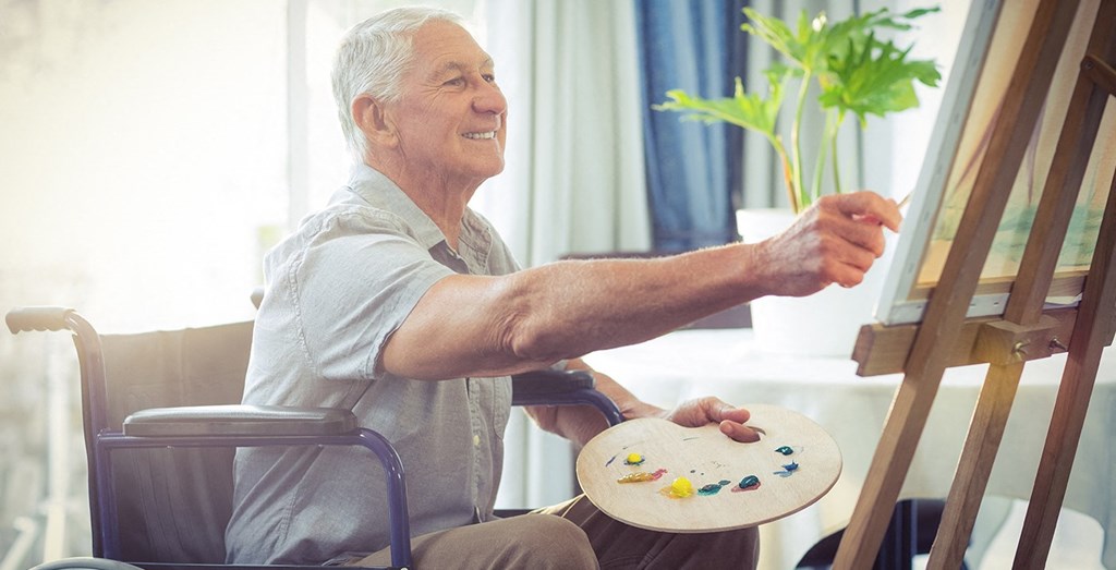 an older man sitting in a wheelchair painting on his art easel