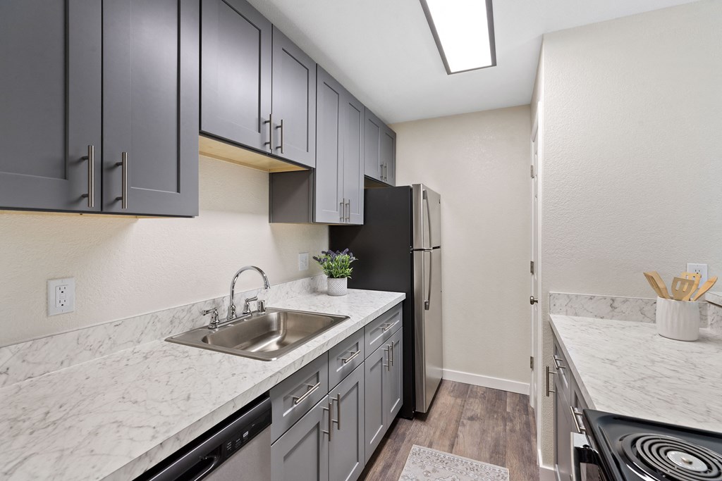 Apartment kitchen with grey overhead cabinetry, plank flooring, and lighting Apartment kitchen with grey overhead cabinetry, plank flooring, and lighting at Hill Crest Apartment Homes, WA 98126