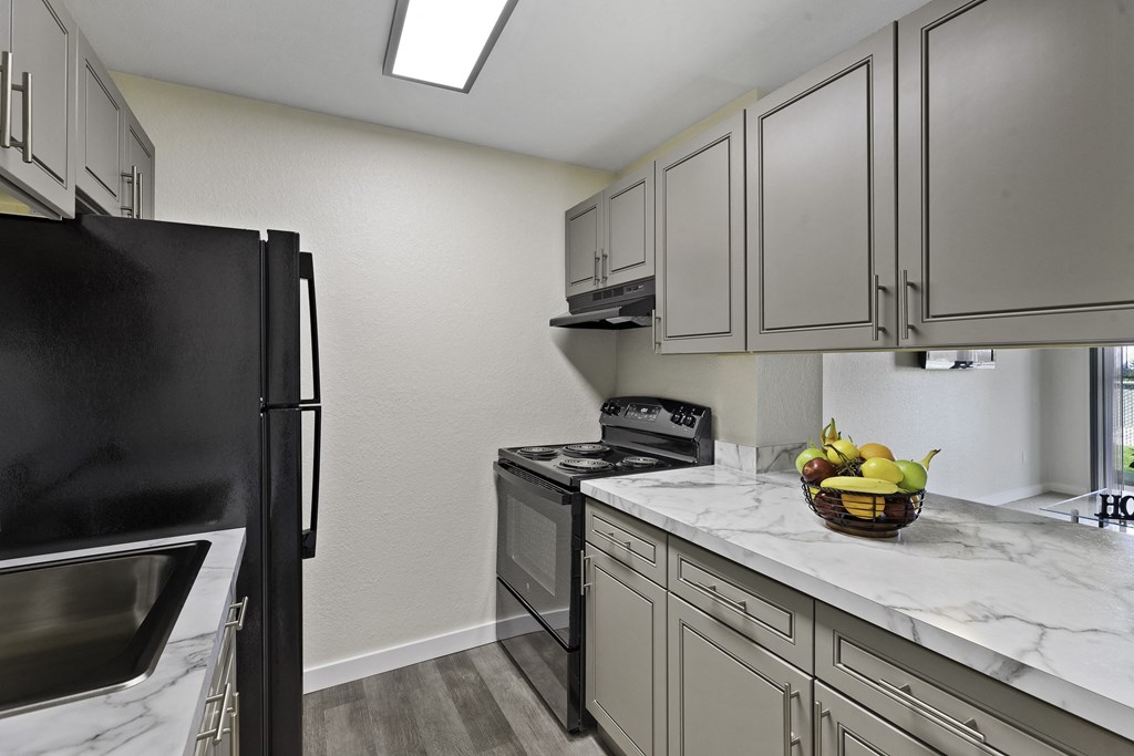 Kitchen with Grey Cabintery, Plank Flooring, and Efficient Appliances, Providing View into Spacious Living Area at Campo Basso Apartment Homes, Lynnwood, 98087