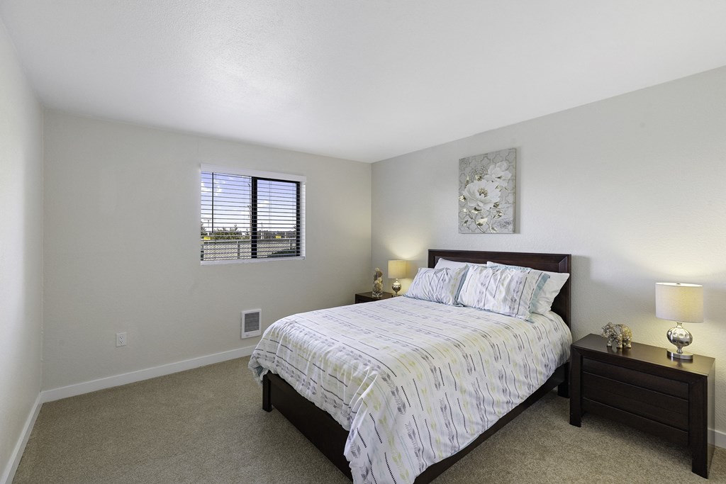Bedroom with a Large Bed and Two Nightstands, Tan Carpeting, and Window at Campo Basso Apartment Homes, Lynnwood