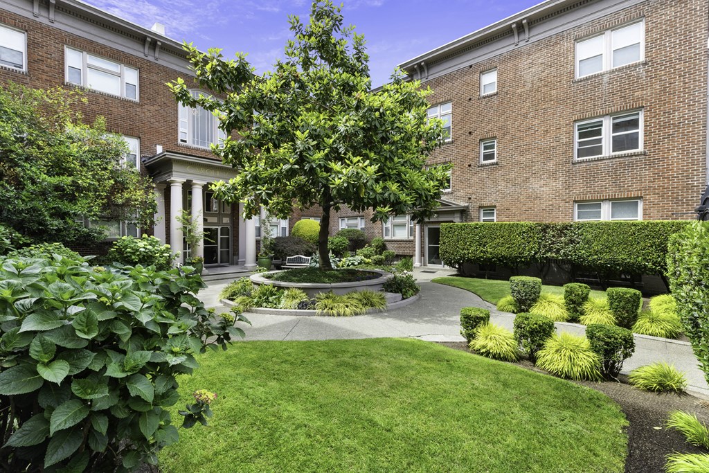 Manicured Courtyard with Tall Tree and Bushes in Front of a Brick Apartments at Carolina Court, Seattle, 98109