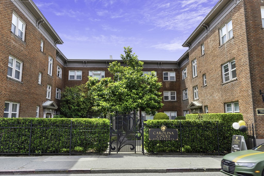 Red Brick Apartment Building with a Black Iron Gate Covered in Greenery and a Center Tee in the Courtyard at Carolina Court, Washington, 98109