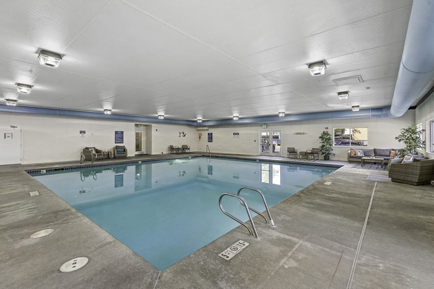 a swimming pool with chairs and tables around it a swimming pool with chairs and tables around it at Camelot Apartment Homes, Everett, WA, 98204 - Photo Gallery