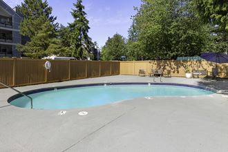 a pool with a fence around it and trees in the background a pool with a fence around it and trees in the background at Casa Blanca Apartment Homes, Everett, 98204 - Photo Gallery