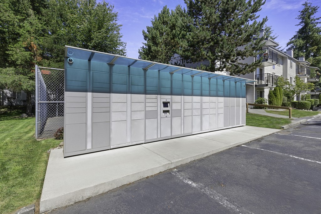 Outdoor Package Receiving Station with Parking Spots and Trees in the Background at Casa Blanca Apartment Homes, Everett, Washington