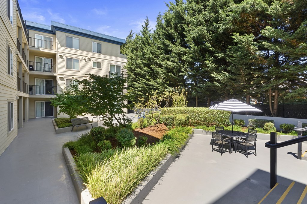 a courtyard with shaded area and a table and chairs with an umbrella at Guinevere Apartment Homes, Washington