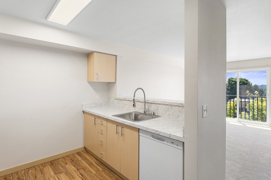 a kitchen with plank flooring, a sink, dishwasher, and natural light from the sliding glass doors at Guinevere Apartment Homes, Seattle, WA