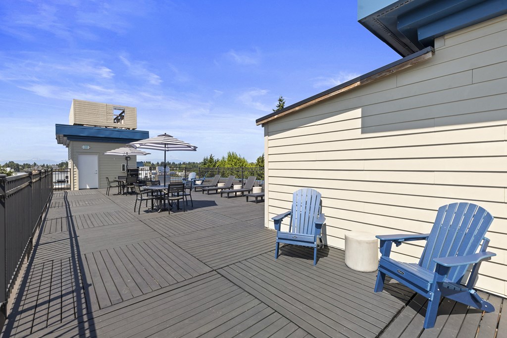 a large Rooftop Resident Lounge deck with blue Adirondack chairs and umbrellas at Guinevere Apartment Homes, Washington, 98103