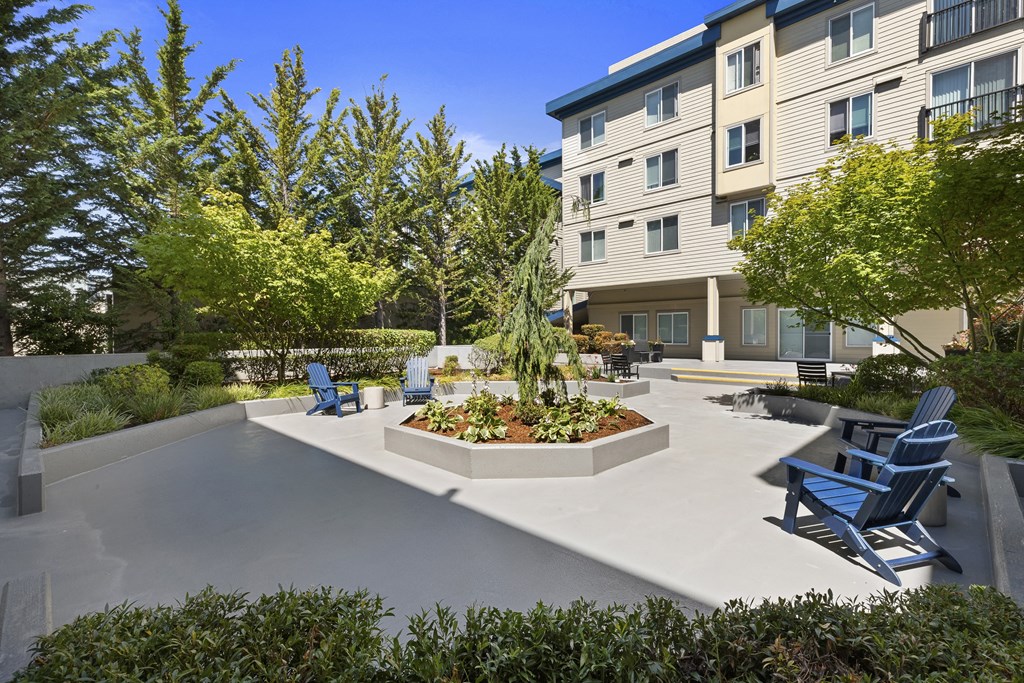 a courtyard with a large tree in the center and a seating areas with blue Adirondack chairs at Guinevere Apartment Homes, Seattle