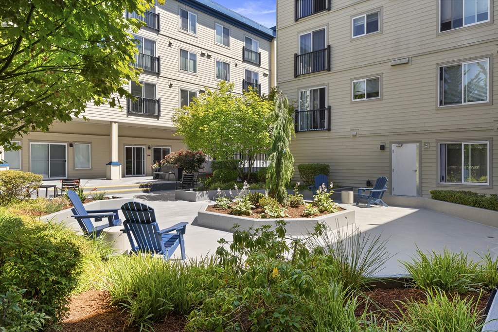 a courtyard with a large tree in the center and Adirondack chairs in front of the property building at Guinevere Apartment Homes, Seattle, 98103