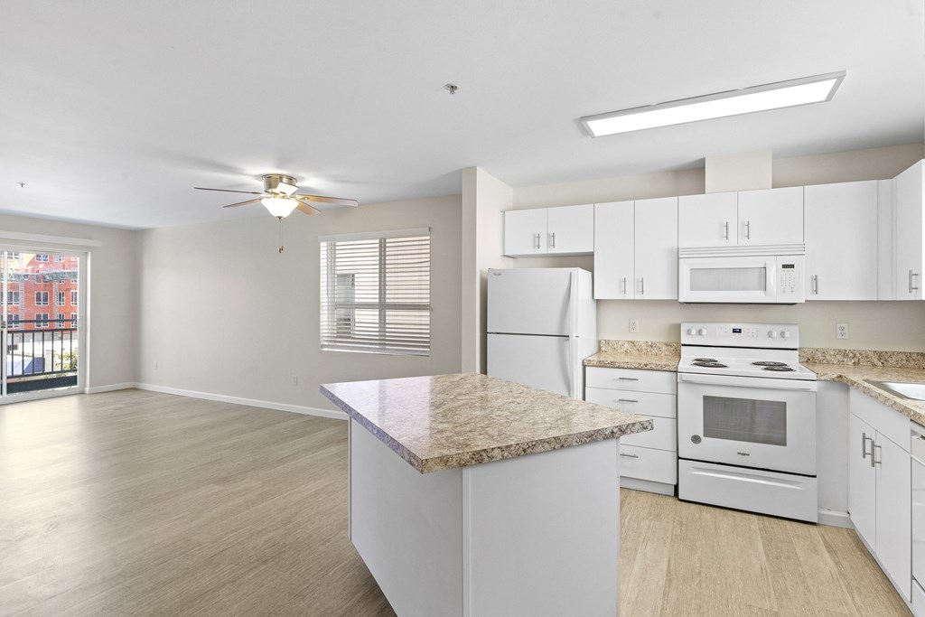a kitchen with white cabinets and a white stove top oven with a view into the spacious living room with plank flooring at Promenade at the Park Apartment Homes, Washington