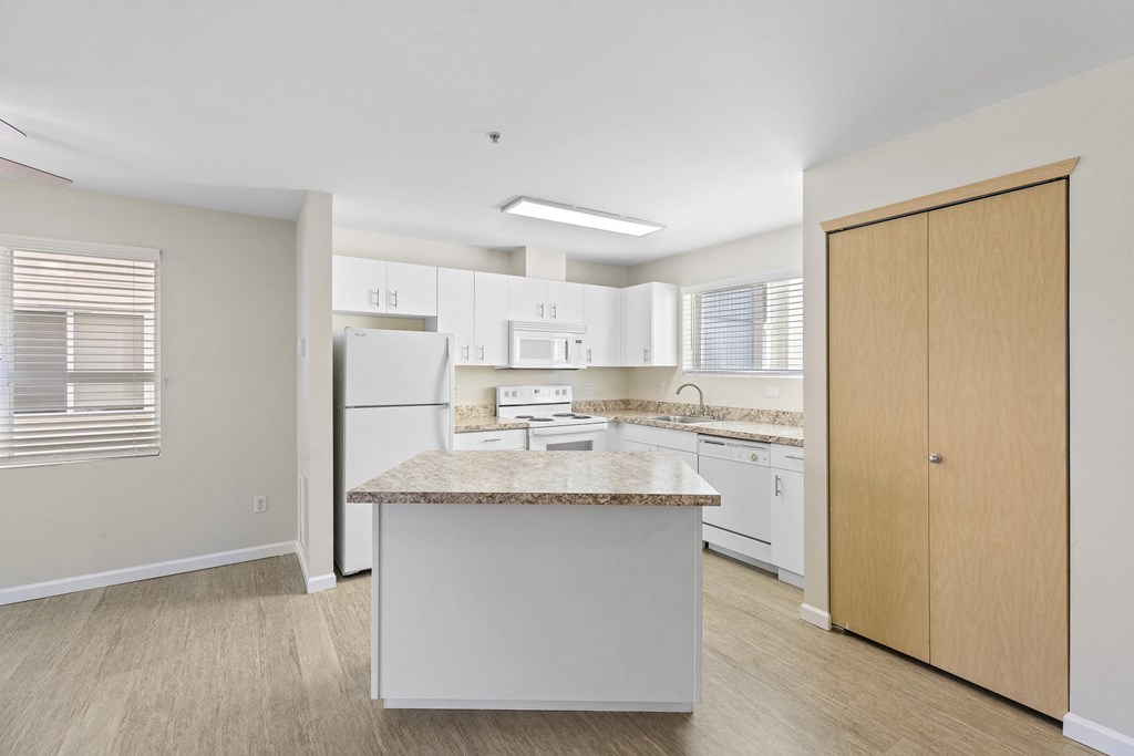a kitchen with an island, plank flooring, overhead lighting, and white appliances at Promenade at the Park Apartment Homes, Seattle