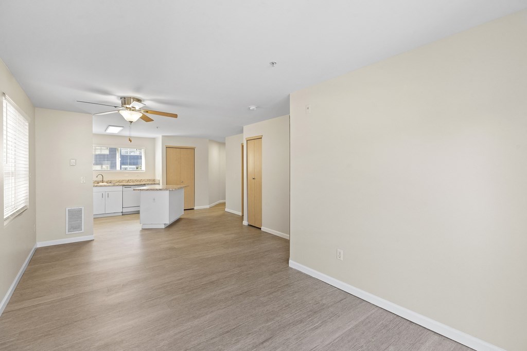 a spacious unfurnished living room with plank flooring and kitchen with an island in the background at Promenade at the Park Apartment Homes, Washington, 98125