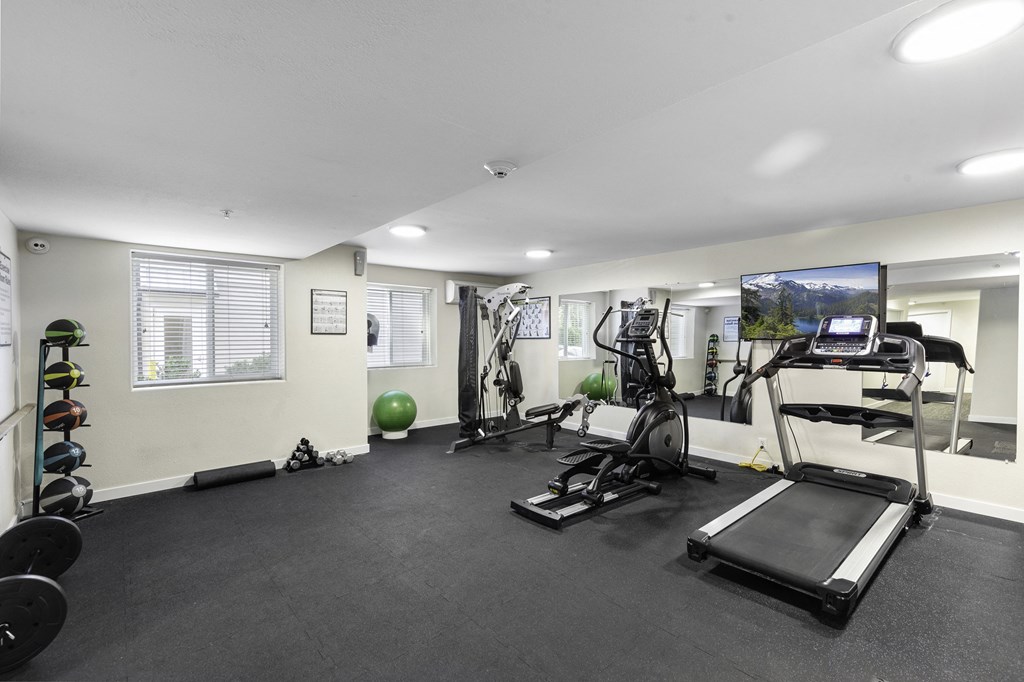 a gym with exercise equipment and a flat screen tv at West Mall Place Apartment Homes, Everett, WA