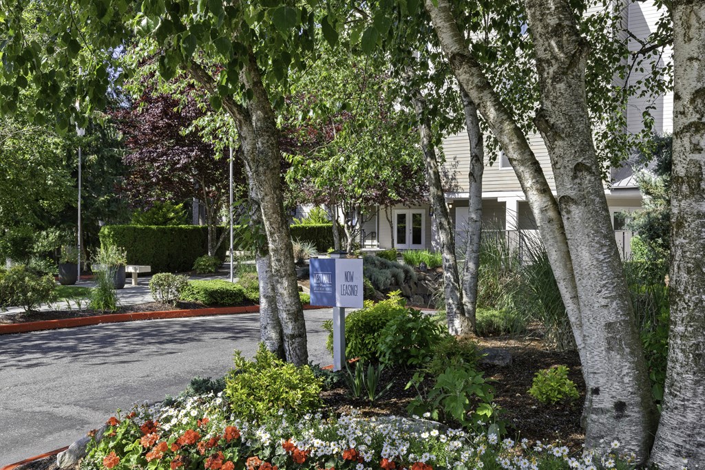 Entrance with trees and flowers in front of property building at West Mall Place Apartment Homes, Everett, WA