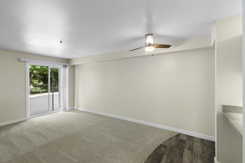 Spacious living room with a ceiling fan with light, cozy carpeting, and sliding glass doors leading to balcony at West Mall Place Apartment Homes, Everett, Washington