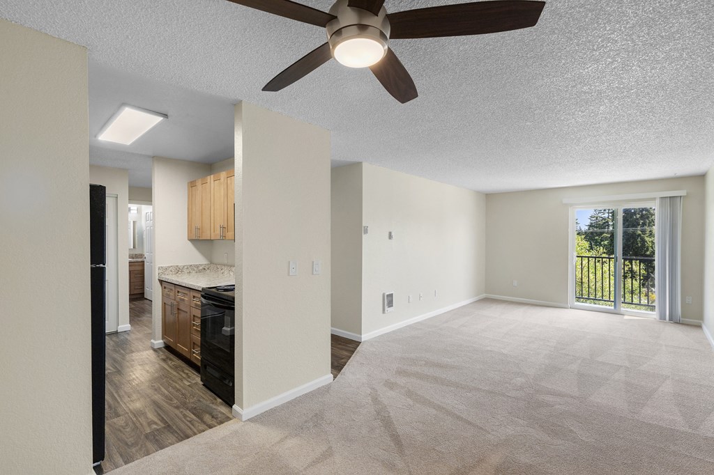 a carpeted living room with a ceiling fan and view of kitchen in the background at Park Edmonds Apartment Homes, Edmonds, 98026