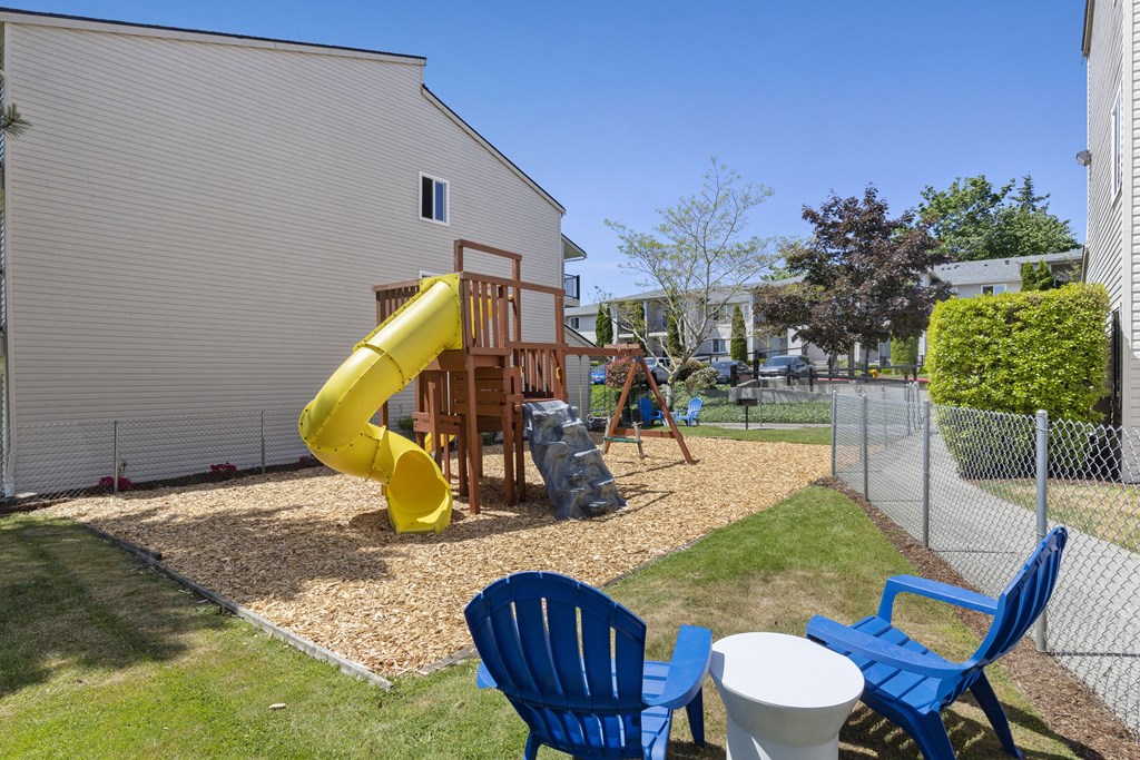 Property playground with a yellow slide in the middle with blue chairs and a table for supervision at Park Edmonds Apartment Homes, Edmonds