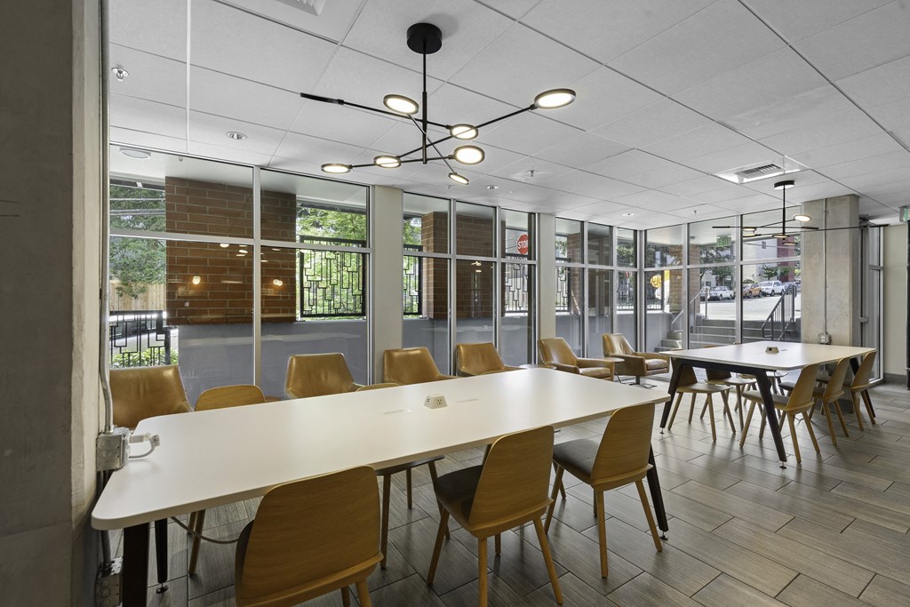 Resident Lounge Space with long white tables, yellow chairs, large windows, and artsy pendant lighting at Sedona Apartments, Seattle, WA, 98115