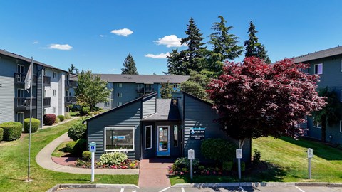 A small building with a blue door is surrounded by greenery and other buildings.