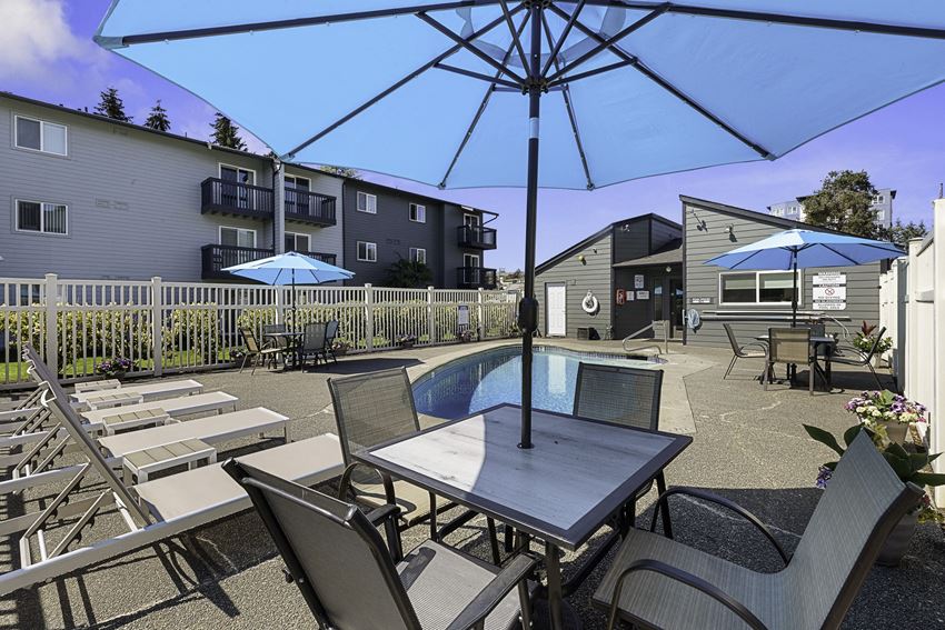 a patio with a pool and chairs and umbrellas a patio with a pool and chairs and umbrellas at Pacific Park Apartment Homes, WA 98026 - Photo Gallery