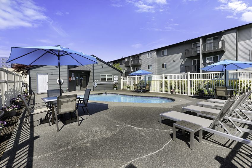 a patio with a pool and chairs and umbrellas a patio with a pool and chairs and umbrellas at Pacific Park Apartment Homes, Washington - Photo Gallery
