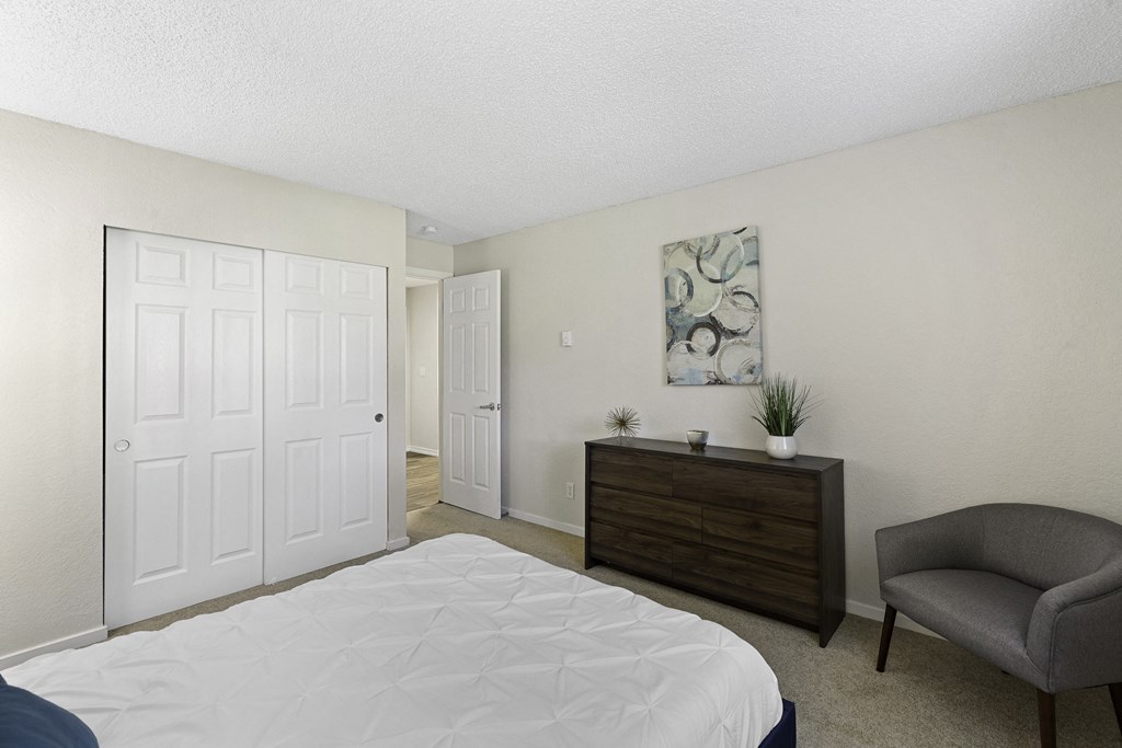 A Spacious Bedroom with a White Bed and a Brown Dresser Beside Two Large White Closet Doors at Pacific Park Apartment Homes, Washington