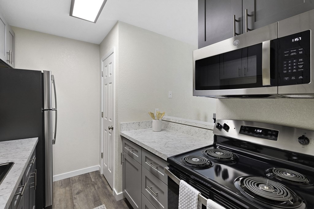 Modern Kitchen with Stainless Steel Appliances, White Countertops, and Plank Flooring at Pinewood Square Apartment Homes, Lynnwood, Washington 98087