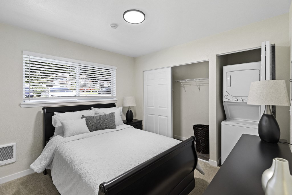 a bedroom with a bed and a dresser with a washer and dryer a bedroom with a bed and a dresser with a washer and dryer at Pinewood Square Apartment Homes, Lynnwood, Washington 98087