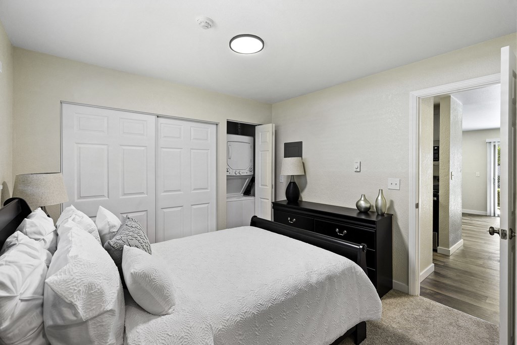 Cozy Bedroom with White Bed facing the Dresser and Large Closet doors, and overhead Lighting at Pinewood Square Apartment Homes, Lynnwood, 98087