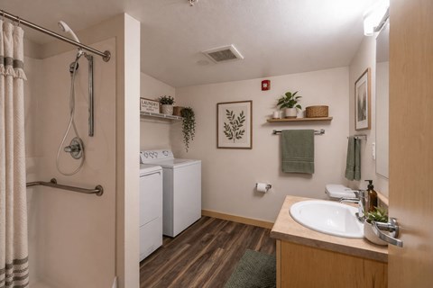 A bathroom with a white washer and dryer, a wooden vanity, and a green towel.