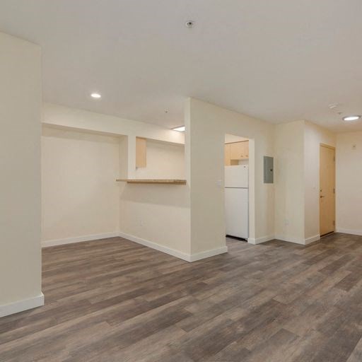 an empty living room with a kitchen in the background an empty living room with a kitchen in the background