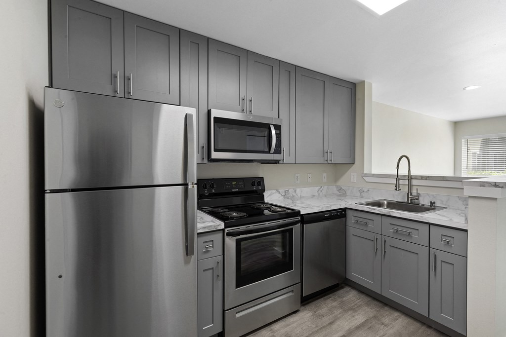 a kitchen with gray cabinets and stainless steel appliances at Excalibur Apartment Homes, Washington, 98004