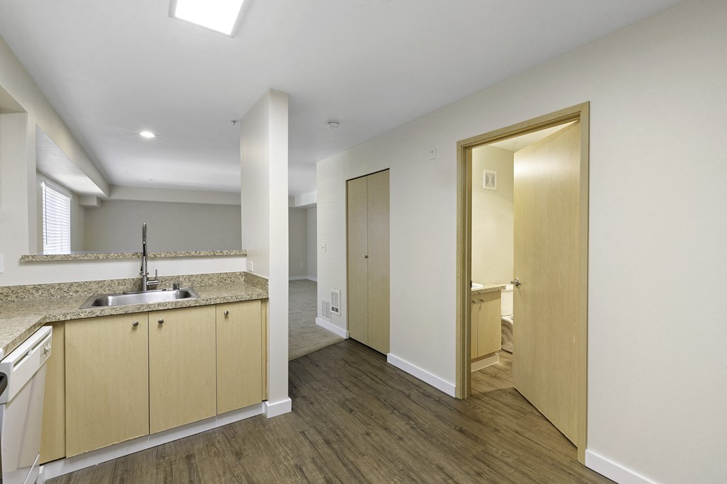 Kitchen View of sink  with Tan Undercabinet, Plank Flooring, and Slight View of Bathroom with Mounted Mirror at Excalibur Apartment Homes, Washington