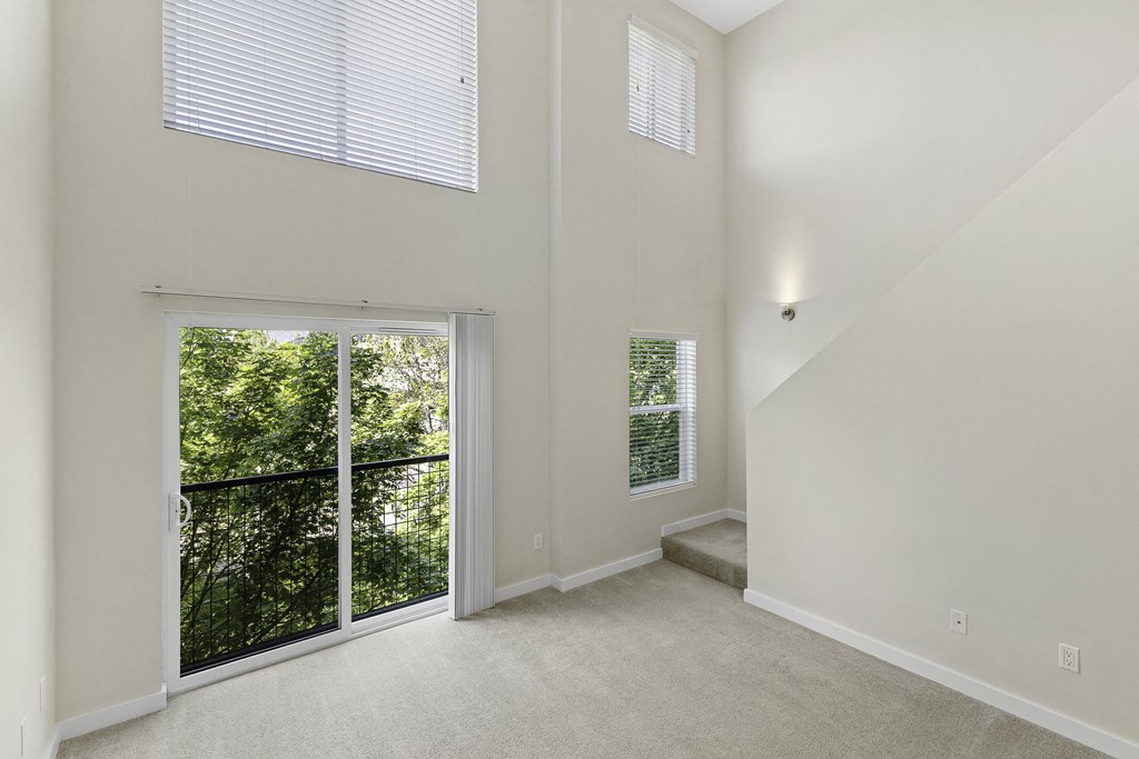 A Two-Story Loft Style Apartment with Living Area that inlcudes Large Windows and Sliding Glass Doors Leading to Outdoor Space at Sir Gallahad Apartment Homes, Bellevue, WA