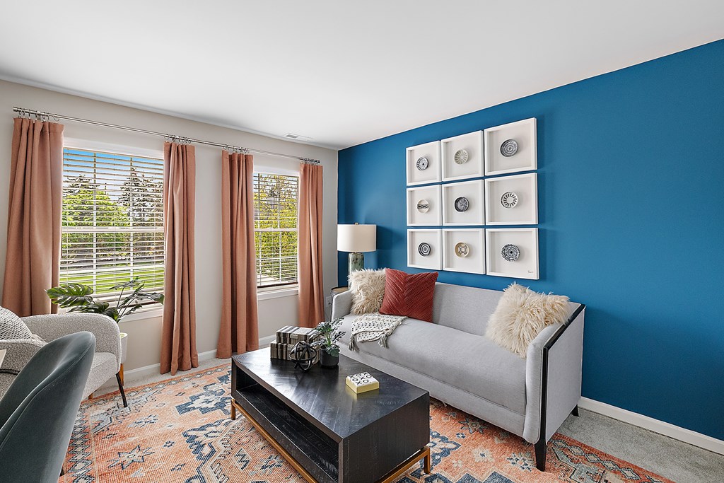 A living room with a grey couch, a coffee table, and a window with curtains.