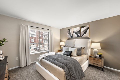A bedroom with a large bed and a window with white curtains.