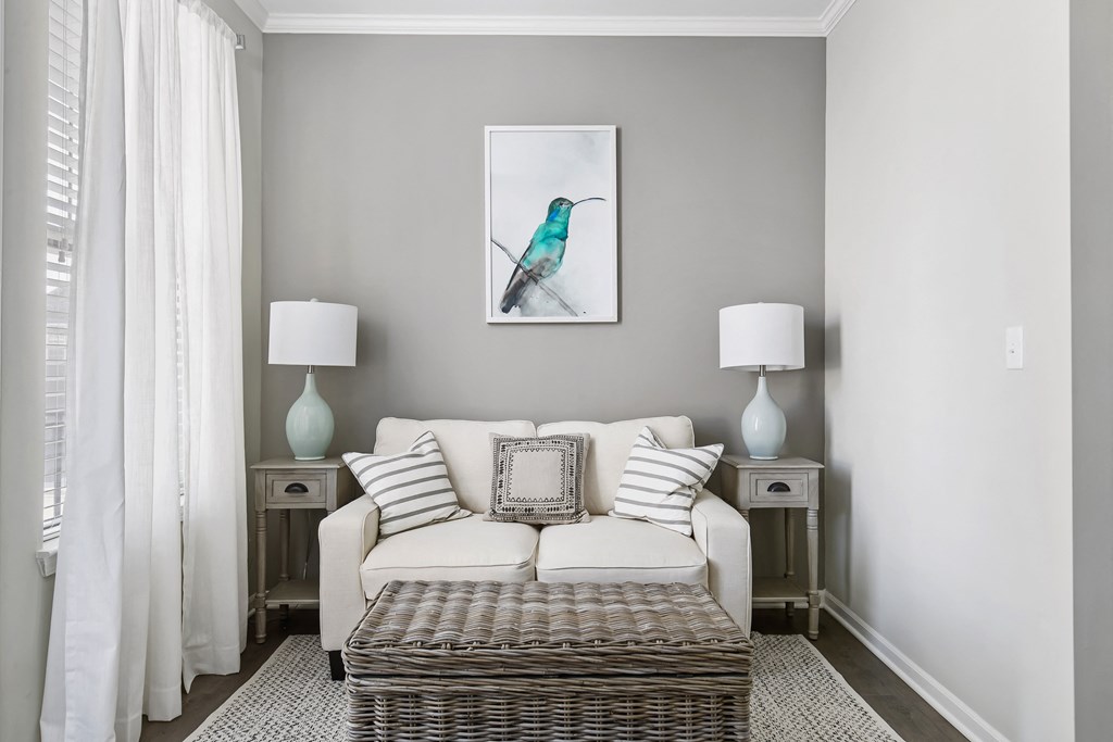 A living room with a white couch, a wicker coffee table, and a painting of a bird on the wall at Park West, Canton, 48187