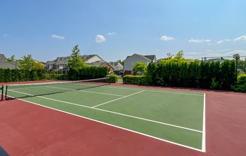a tennis court with houses in the background on a sunny day at Cidermill Village Apartments in Rochester Hills, MI 