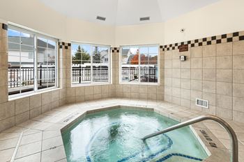 A hot tub in a room with a view of a fence and trees outside.