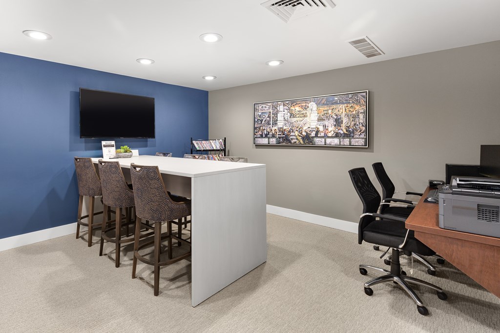 A room with a bar and chairs, a television, and a painting on the wall.