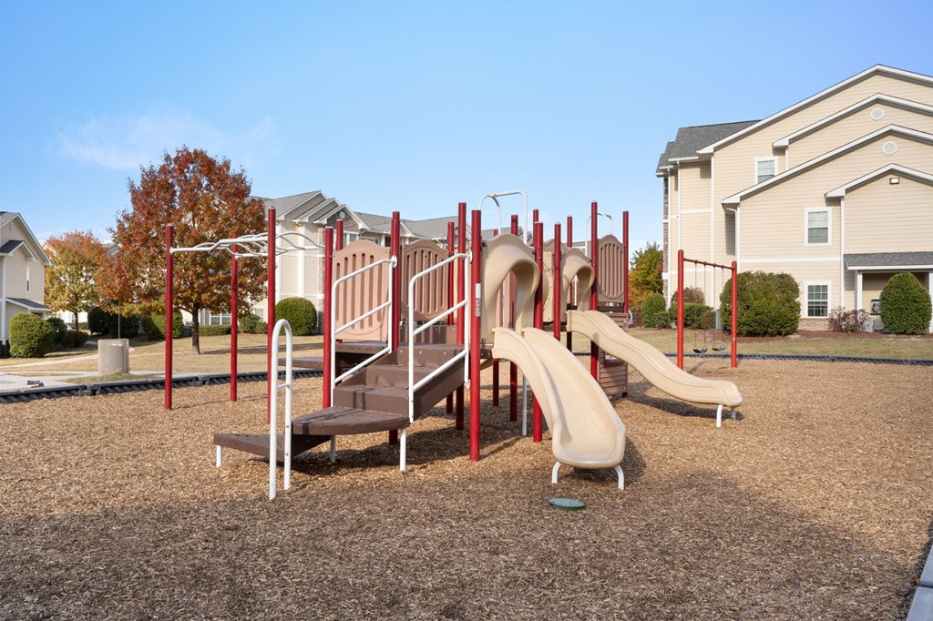 A playground with a red slide and a brown bench.