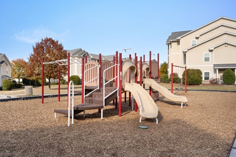 A playground with a red slide and a brown bench.