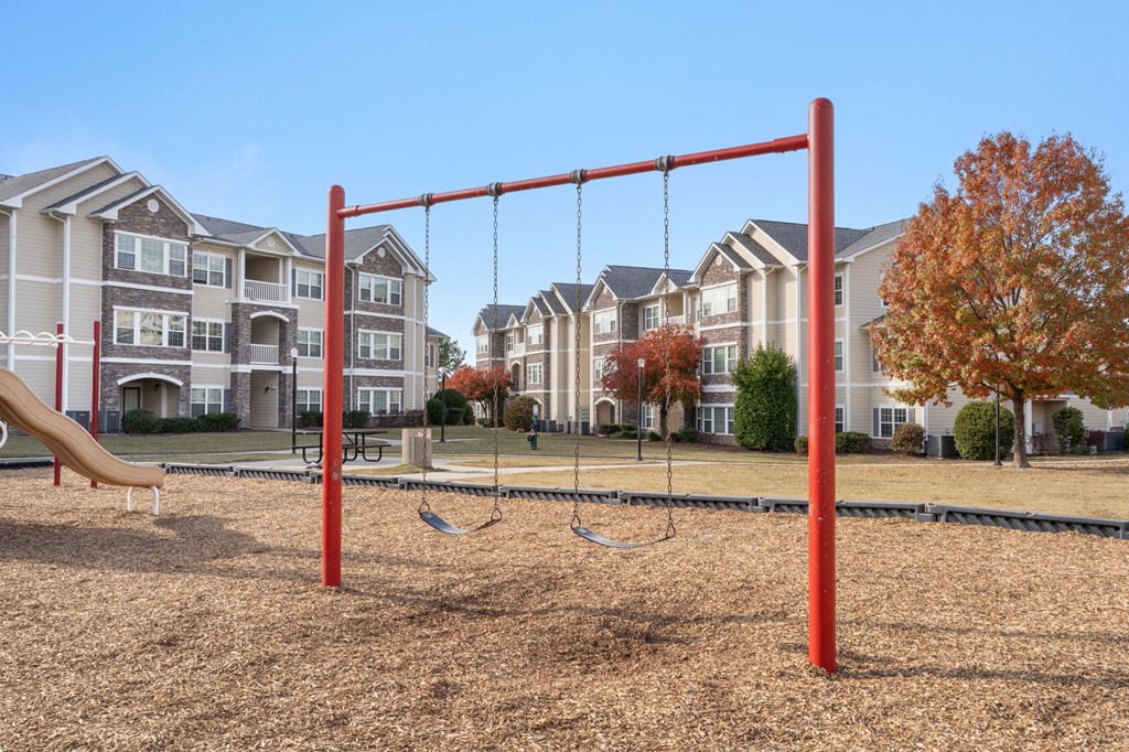 A playground with a red swing set in front of apartment buildings.