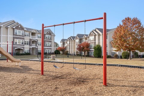 A playground with a red swing set in front of apartment buildings.