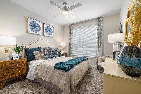 A bedroom with a bed, a ceiling fan, and a side table with a vase.