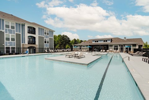 A large swimming pool in front of a building with a poolside lounge.