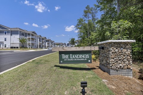 A sign for The Landings at Hard Scrabble is in front of a stone wall.
